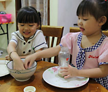 兩隻小手在碗裡鉆動，握一把米，存入奶瓶裡的是米粒，還有滿滿的愛心。（左：莊禾靖、右：莊禾群）【攝影者：莊濟智】