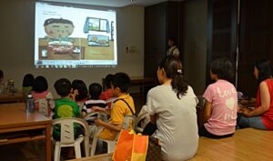 透過投影機，孩子們在台下聼老師導讀《我吃拉麵》的繪本。【攝影者：陳志財】