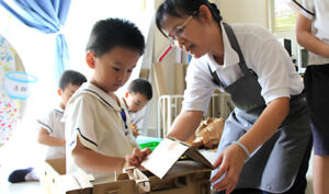 王淑惠老師（左二）細心引導謝啟航小朋友（左一）如何建設用愛打造的學校。【攝影者：胡慧芬】