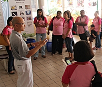 一群身穿粉紅制服的D'monte 幼兒園老師,聚集在慈濟環保教育站聆聽慈濟志工蕭益光（左一）給予的環保講解。【攝影者：胡慧芬】