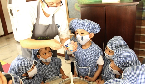 幼兒園園長譚莉蓮（慈遵）教導小朋友把材料放進攪拌碗。【攝影者：楊雪琳】
