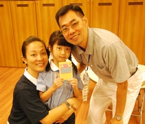2013年，周巧善在人文學校課上製作父親節卡片給爸爸周發順，開心地與父母一起示出卡片。【攝影者：余康立】