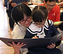 媽媽王進雲抱著孩子蘇睿儀一起觀看園長分發的畢業證書。【攝影者：王秀蘭】