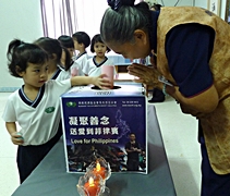 四歲大爱班的赖珈妤將平日存進奶瓶撲滿的善款，投入愛心箱裡。【攝影者：萧依玲】