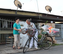 馬瑞蓮師姊將家裡的舊報紙遞給騎單車到鄰家收集資源的茹澤響師伯。【攝影者：陳韻如】