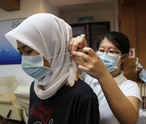 護士羅絲娜妮（Rosnani bt Mat Isa）戴著髒手套不便戴口罩，培訓中的護士張旖潔出手協助。【攝影者：顏如艷】