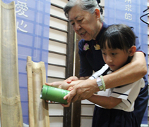 園長吳芳英（慈僖）協助小朋友們把竹筒內的錢幣投進甕裡。【攝影者：翟佩庭】