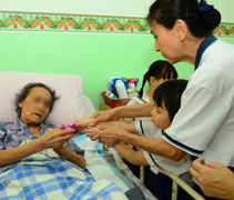 老師握著小朋友的手，讓小朋友把胡姬花交到臥在床上的老菩薩。【攝影者：許名傳】