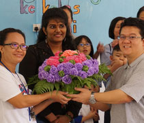 家長們將一束用塑料袋和香蘭葉製作了環保玫瑰，獻給物理治療師莎茜蕾卡（中）和手工老師芭琳逹（左），同理他們在工作時的辛苦和付出。【攝影者：王欐樺】