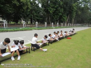 一张长凳，一张画纸与一盒蜡笔，孩子们蹲在草地上hu绘出美丽的教育中心。